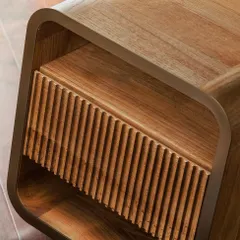 This bedside table features a fluted drawer front set within a gently curved metal and wood frame. The combination of sharp, vertical lines and soft, rounded corners creates a balanced and sophisticated piece.