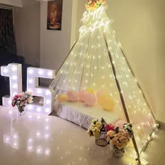 A dreamy 16th birthday setup featuring a beautiful teepee tent adorned with fairy lights. Large light-up marquee numbers '16' add to the celebratory feel.