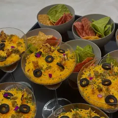The first course: a deconstructed layered Mexican dip served in elegant glassware with colorful spinach and beetroot nachos.
