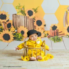 A cheerful baby boy dressed in bright yellow sits in a basket surrounded by sunflowers and cute bee decorations, creating a sunny and happy "bee-themed" photoshoot.