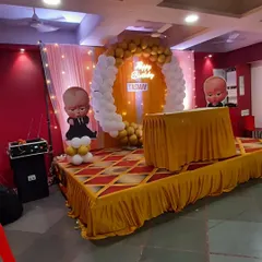 A 'Boss Baby' themed birthday stage. The gold and white balloon arch and character cutouts create a fun and stylish backdrop for the cake cutting ceremony.