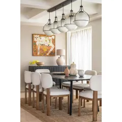 The dining room in Apartment 1600 captures a sense of tropical luxury. A dark wood table is paired with unique, block-legged chairs and a statement pendant light, with vibrant artwork adding a splash of color to the serene space.
