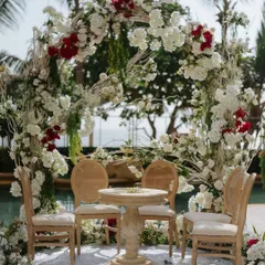 A close-up of an intimate mandap setup by the pool, featuring a deconstructed arch of white and red flowers. The organic, free-flowing floral design creates a romantic and natural frame for the ceremony, perfect for a modern garden wedding.