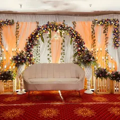 A rustic yet elegant reception stage. This design features a floral arch with orange drapes, complemented by wooden crates and bouquets of flowers, creating a warm and charming look.
