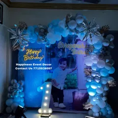 A cool blue and silver themed decor for a first birthday at home. This setup uses a personalized photo backdrop, a balloon arch with starburst foil balloons, and a neon sign.