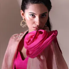 A close-up editorial shot that focuses on structure and color. The vibrant pink sculptural detail on the shoulder contrasts with the soft organza cape, while the sharp winged eyeliner adds a graphic, high-fashion edge.