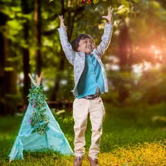 A boy jumps for joy in a green, sunlit park with a teepee in the background. This photo is full of energy and captures the pure freedom of being a kid outdoors.
