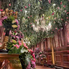 A side view of the entrance passage, showing the sheer density of the floral arrangements. The combination of a lush green ceiling, hanging pink roses, and large floor bouquets created a multi-layered, immersive floral experience.