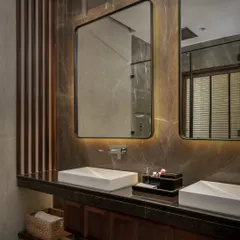 An organic, warm bathroom with earthy brown stone walls and LED backlighting behind the mirrors. A tucked-in sculpture adds a curated, personal touch to this immersive space.