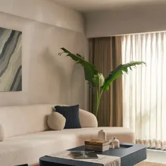 An ivory boucle sofa sits against a light grey lime-washed wall, creating a soft and inviting corner. The abstract art adds a touch of modern personality to the serene, minimalist living room design.
