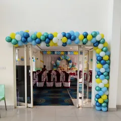 This L-shaped balloon arch frames the doorway into a hall, using a playful mix of blue, yellow, green, and white. It's a great way to guide guests and add a splash of color.