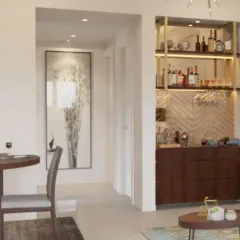 This compact home bar is cleverly integrated into the living area. It features a herringbone backsplash, rich wood cabinetry, and open shelving with gold accents, proving that you don't need a large space to have a stylish bar.