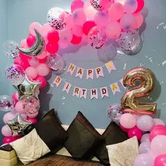 A vibrant pink birthday decoration set up behind a sofa. The balloon arch is filled with shades of pink, confetti balloons, and star and moon foil balloons, perfect for a second birthday.