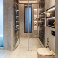 This bathroom design balances light and dark marble for a sophisticated contrast. The walk-in shower is framed by glass, and recessed, backlit niches provide elegant storage for toiletries.
