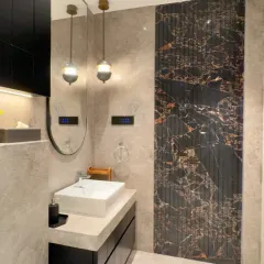 This bathroom combines classic and modern elements. A dark, fluted marble panel creates a dramatic accent wall behind the sink, while minimalist pendant lights and a sleek vanity complete the sophisticated look.