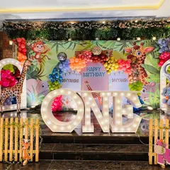 A vibrant and colorful jungle safari stage for a first birthday, packed with animal characters, balloon garlands, and large "ONE" marquee letters.