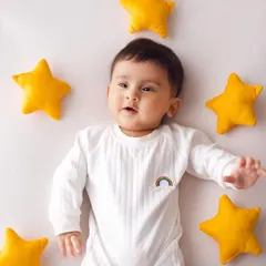 A creative five-month-old portrait with the baby lying on a white background surrounded by plush yellow stars, looking up as if dreaming.