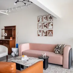 This living area is a study in balancing forms and colors. The custom pink sofa with its curved silhouette is set against a gallery wall of abstract art, while a vintage wooden cabinet adds a touch of history. The space feels curated, personal, and full of character.