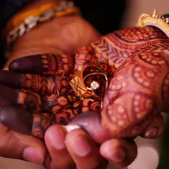 A powerful and intimate shot of the bride and groom's hands, showcasing the deep, dark stain of the bride's mehendi as she holds the wedding ring.