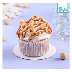 A close-up of my Biscoff Hazelnut cupcake, topped with cream, caramel drizzle, and crunchy toasted hazelnuts.