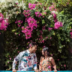 A vibrant and joyful moment under a canopy of bougainvillea flowers. The falling petals add a touch of magic to this colorful and happy couple portrait.