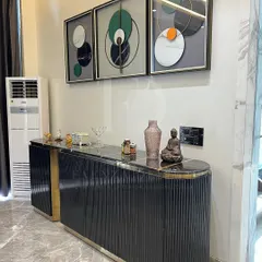 A modern console unit in black and gold. The piece features a fluted design on the doors, a black marble top, and a sculptural gold-finished base, making it a glamorous addition to any entryway or living room.