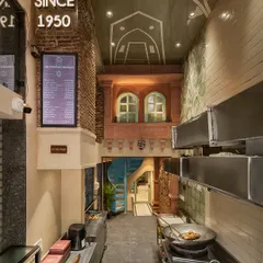 Another view of the Shiv Mishthan Bhandar interior, showing the interplay of exposed brick, a painted ceiling echoing traditional motifs, and a modern menu board. The design creates a layered experience in a narrow space.