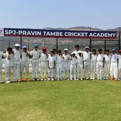 A junior team stands proudly on the field for a photo, with the practice nets and our academy banner visible behind them.