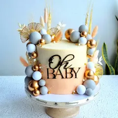 An elegant and modern baby shower cake. This design features a two-tone buttercream finish, decorated with chocolate spheres and dried botanicals for a trendy, boho-chic look.