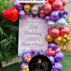 A personalized welcome stand for Manju and Mahesh's 25th wedding anniversary. The sign is framed by a colorful balloon garland that matches the main party decor, welcoming guests to the celebration.