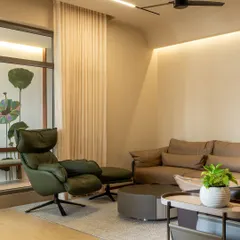 A cozy corner of the living room, featuring a comfortable green leather recliner and ottoman. Soft, layered lighting and sheer curtains create a perfect spot for relaxation.