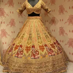 A multi-toned gold bridal lehenga with intricate red and green patterns. This view shows the full, regal flare of the skirt.