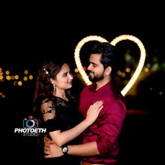 A beautiful nighttime couple portrait with a softly lit heart in the background. The bokeh effect from distant lights adds a dreamy quality to the image.