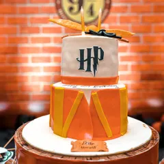 A magical Harry Potter themed cake. This two-tiered creation is designed to look like a drum from the Hogwarts marching band, complete with the HP logo and a golden snitch on top.