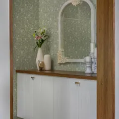 The foyer in 'House of Kismish' exudes Victorian grace with its subtle wallpaper, distressed wall mirror, and a floating shoe cabinet that cleverly conceals the DB board.