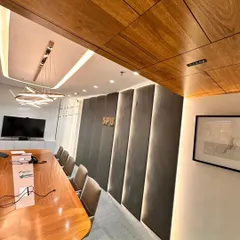 This shot highlights the material palette of the boardroom. The contrast between the warm wood ceiling panels, the soft grey acoustic wall, and the sleek white cabinetry creates a balanced and professional atmosphere.