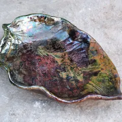 The magic of Raku firing. This leaf-shaped platter started as plain clay and was transformed by fire and smoke into this iridescent, unpredictable piece of art. This is what happens when you let the process have a say.