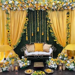 A beautiful Mehendi seating arrangement with a backdrop of yellow drapes, a green foliage wall, and sunflower accents.
