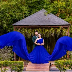 This dramatic shot uses a long, flowing blue gown to create a sense of grandeur. The couple stands on a wooden gazebo, surrounded by greenery, making for a stunning pre-wedding photograph.