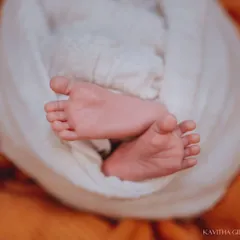 Another adorable shot of tiny feet, this time peeking out from a white swaddle against a warm orange blanket. The contrast in colors makes the details pop.