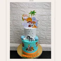 A wild jungle adventure for Jodhpreet's birthday. This two-tiered cake is decorated with friendly fondant animals, a zebra, and cute cartoon toppers, perfect for a safari-themed party.