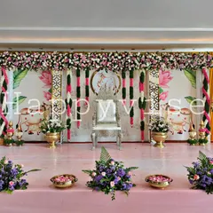 A complete stage setup for a baby shower or naming ceremony with a traditional Indian theme. The backdrop features cow and lotus motifs, complemented by fresh flower arrangements and a silver throne chair.