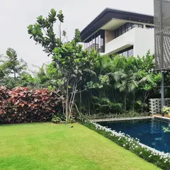 I design and maintain gardens that seamlessly integrate with your home's architecture. This villa backyard at Embassy Boulevard features a pristine lawn that meets the edge of a swimming pool, complemented by a vibrant red-leafed hedge and tropical foliage.