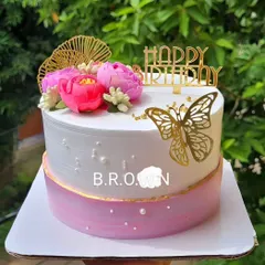 A beautiful and elegant birthday cake. The design combines a pink and white ombre effect with fresh pink flowers, a gold butterfly, and a "Happy Birthday" topper.