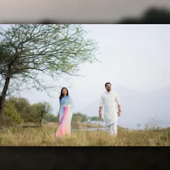 A wide shot showing the couple in traditional wear walking through a field, blending cultural elegance with natural beauty.