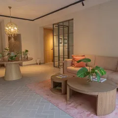 Another view of the office lounge, showcasing the herringbone patterned floor and the comfortable seating arrangement. The space is designed with a mix of textures, from the soft rug to the wooden coffee tables, creating a warm and inviting atmosphere for visitors and employees.