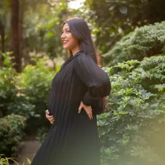 The expecting mother is captured in beautiful side-profile light, smiling as she looks into the distance. This shot highlights her happy glow against a garden backdrop.