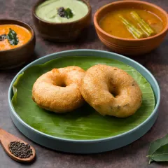 A classic Medu Vada shot, styled traditionally on a banana leaf with accompanying chutneys and sambar. This type of authentic presentation helps build trust and appeal for South Indian restaurants.