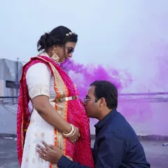 A beautiful maternity portrait using a vibrant purple smoke bomb for a dramatic effect. The father-to-be kisses the baby bump, creating a touching and artistic image.