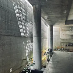 A wider view of the same space, revealing the relationship between the structural columns and the wall. The shadows cast by the overhead grille add a layer of texture and complexity to the minimalist material palette.